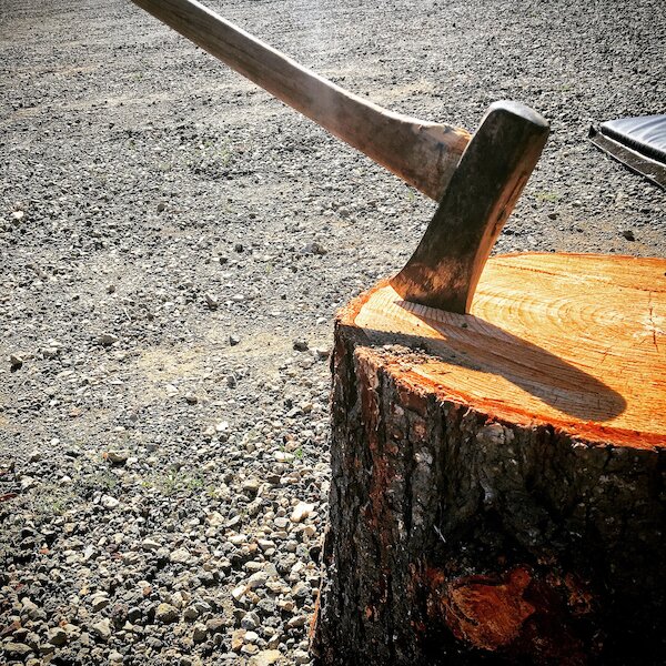A splitting maul that is stuck in a round of wood.