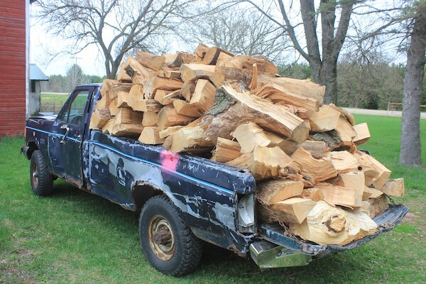 A truck that is haphazardly filled with firewood. The wood is just thrown in the bed; if it were stacked properly, more wood could be fit.